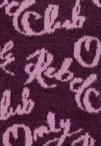 Primer plano de una tela de punto púrpura con patrones de texto en cursiva rosa integrados en la textura.