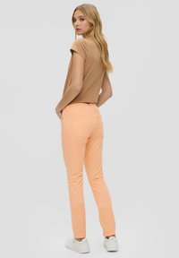 Lichtgewicht tan t-shirt en perzikkleurige slim-fit jeans. Jeans hebben achterzakken en een gladde textuur. Witte sneakers maken de outfit compleet.