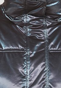 Svart puffjacka med en glänsande, mjuk textur. Har en hög krage och subtila sömmar på framsidan. Lätt och isolerad.