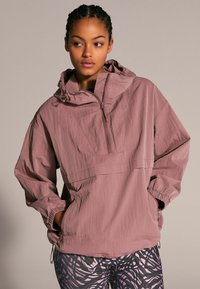 Giacca leggera color malva con zip a metà, cappuccio e polsini elasticizzati. Abbinata a leggings con motivo caratterizzato da vortici neri e rosa.