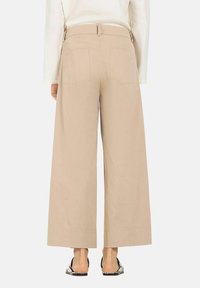 Beige wide-leg trousers with a high waist, two back pockets, and a smooth texture, paired with open-toe sandals.