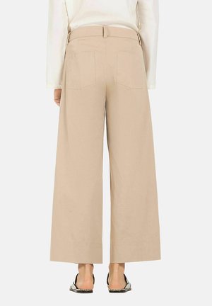 Beige weite Hose mit hohem Bund, zwei Gesäßtaschen und glattem Material, kombiniert mit offenen Sandalen.