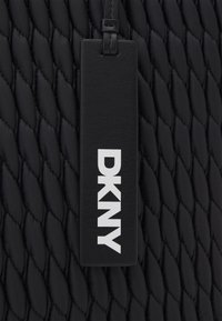 Sac matelassé noir en matériau texturé. Étiquette en cuir intégrée affichant "DKNY" en lettres blanches en gras.