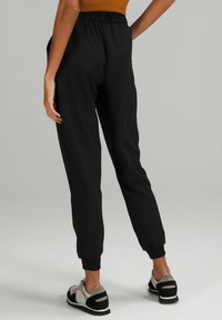 Czarne dresy z elastycznym pasem i ściągaczami. Gładka faktura materiału. Model nosi szare i czarne buty sportowe.
