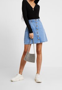 Ljusblå denim A-linje kjol med knappstängning fram, kombinerad med en figurnära svart ribbad topp och vita sneakers. Liten texturerad handväska.