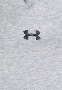 Grå bomullstyg med en subtil textur; har en mörk broderad Under Armour-logotyp på övre vänstra sidan.