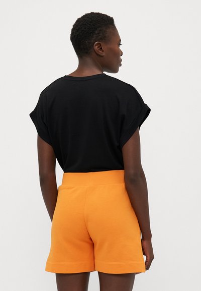 Black relaxed-fit t-shirt with rolled sleeves paired with orange cotton shorts featuring a wide elastic waistband and stitched hem.