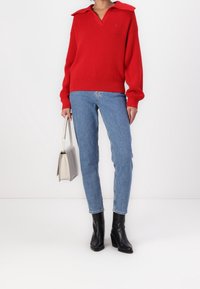 Red knit sweater with a large collar, paired with light blue denim jeans and black ankle boots. Holding a pale gray handbag.