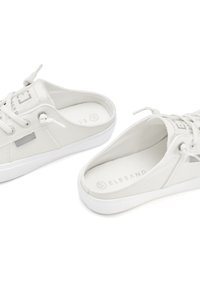 White canvas sneakers with round toes, flat white rubber soles, and light grey accents. Features lace-up closure and textured fabric.