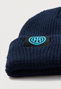 Gorro de malha azul-marinho com textura canelada, com vira e um rótulo preto com um logótipo azul na frente.