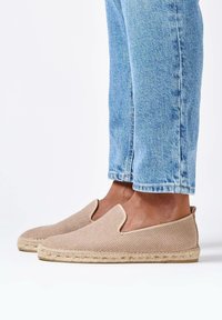 Beige espadrilles zonder hiel met een geweven textuur en een jute touwzool. Gecombineerd met lichtblauwe denim jeans met omslag.