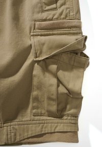 Bézs színű cargo nadrág rövidnadrág több oldalzsebbel, az egyik zseben texturált folttal és masszív varrási részletekkel. Állítható derékpánt látható.