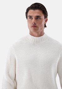 Weißer gestrickter Pullover mit hohem geripptem Kragen und strukturiertem Muster, im lässigen Schnitt und mit langen Ärmeln.