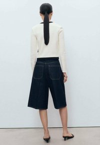 Jeans culottes i mörk tvätt med kontrasterande sömmar, ihop med en krämfärgad långärmad topp och svart midja, med en avslappnad passform.