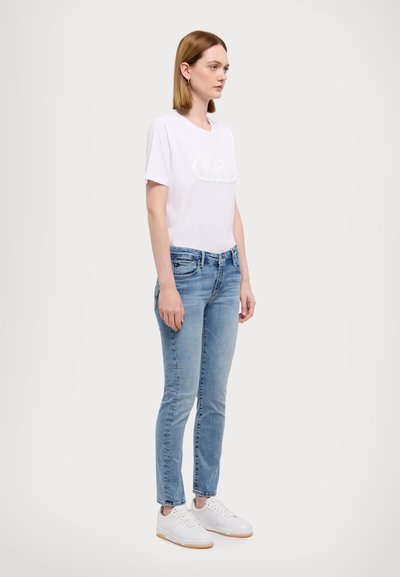 Hvid kortærmet t-shirt med hævet logo, parret med lyseblå slim-fit jeans og hvide sneakers med struktureret sål.