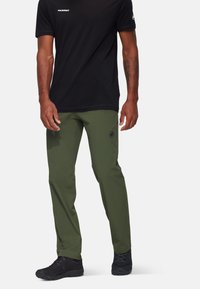 Black short-sleeve shirt with a logo, paired with olive green, lightweight pants featuring an emblem and black athletic shoes.