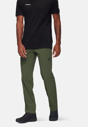 Zwart T-shirt met korte mouwen met een logo, gecombineerd met olijfgroene, lichte broek met een embleem en zwarte sportschoenen.