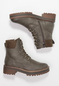 Bottes de cheville en cuir vert olive avec lacets, fermeture éclair sur le côté, accents en daim marron et semelle crantée pour une meilleure adhérence.