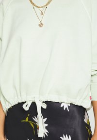 Ljust grön sweatshirt med samlad midja och knytbart dragsnöre, med ribbade ärmslut. I kombination med en mörkblommig kjol.