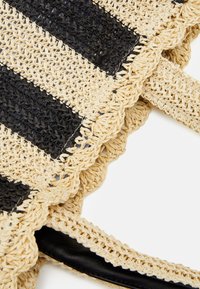 Sac tressé en fibres naturelles tissées, présentant des rayures alternées noires et beiges, avec un bord festonné et des accents de poignées en cuir noir.