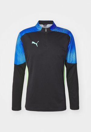 Sportshirt met lange mouwen, featuring een zwart lijf, blauwe patroonschouders en groene accenten. Met ritskraag en Puma-logo op de borst.