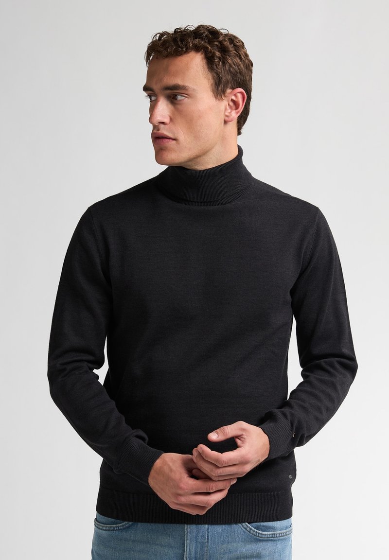 Schwarzer Rollkragenpullover aus glattem Material mit langen Ärmeln und geripptem Kragen, kombiniert mit hellblauen Jeans.