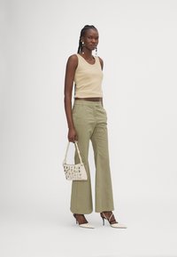 Pantalons larges khaki associés à un débardeur côtelé beige. Les accessoires comprennent un petit sac tissé et des escarpins blancs à bout pointu.