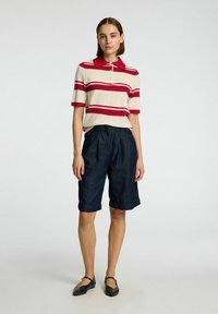 Beige en rood gestreept polo-shirt met een kraag, gecombineerd met donker denim knielange shorts met een relaxte pasvorm en opgerolde mouwen. Zwarte flats.