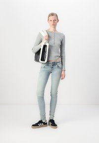 Pelēka ribota garām piedurknēm augšdaļa, gaiši zila slim fit džinsi, melni sporta apavi ar baltām strīpām, tur melnu somu ar baltu mākslīgo vilnu.