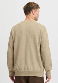 Beige knitted sweater with a crew neck, textured fabric, long sleeves, and ribbed cuffs and hem. Shown from the back, no visible branding.