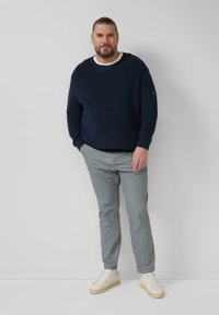 Marineblauwe geribbelde trui met witte kraag, grijze slim-fit broek en witte sneakers met tankleurige zool. Model staat tegen een neutrale achtergrond.