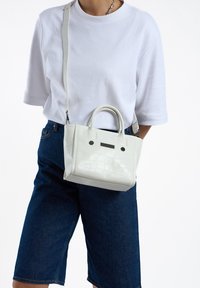 Kleine witte handtas met een textuur en croco-patroon, dubbele handvatten en een verstelbare schouderband voor crossbody gebruik.