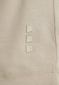 Beige cotton fabric with a ribbed texture. Three square-shaped accents are sewn onto the side, featuring a smooth finish.