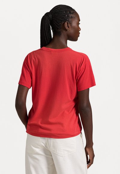 Tricou roșu din bumbac, cu mâneci scurte, gât rotund și o croială lejeră. Prezintă o textură netedă și un design simplu, fără modele vizibile.