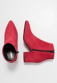 Bottines en daim rouge avec un bout pointu, un talon bloc et une fermeture éclair latérale. Texture lisse et design épuré, adaptées à diverses tenues.