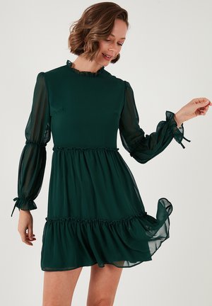 Dark green dress made of lightweight fabric, featuring a fitted bodice, frilled neckline, puffed sleeves, and a tiered ruffled hem.
