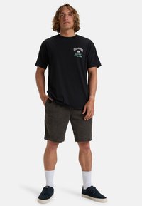 Black cotton t-shirt with front graphic, paired with dark gray shorts, white socks, and navy sneakers. Casual, relaxed fit.