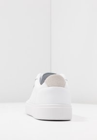 Vit sneaker med övre i slät läder, grå mocka på hälfliken och tjock vit gummisula. Minimalistisk design med perforerad detaljer.