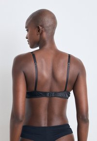 Fekete bikini felső állítható pántokkal, hátul kapoccsal és sima, elegáns textúrával. Egyszerű mintázat nélküli dizájn.