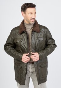 Lederjacke in dunkelolivgrün mit einem braunen Schaffellkragen, ausgestattet mit vier Fronttaschen und einem Reißverschluss. Glatte Textur, lässige Passform.