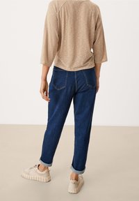 Gestreiftes beige und braunes Oberteil mit Dreiviertelärmeln, kombiniert mit dunkelblauen Jeans, die umgekrempelte Bündchen haben, und weißen Sneakers mit dicken Sohlen.