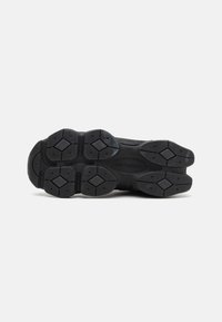 Semelle de sneaker en caoutchouc noir dotée d'un motif texturé avec des formes hexagonales et des diamants, conçue pour l'adhérence et la durabilité.
