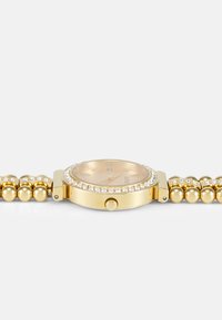 Gold watch with a round face, cream dial, crystal accents, and a beaded gold strap. Features a crown on the side for adjustments.