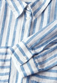 Camicia di lino con strisce verticali blu e bianche. Presenta un colletto e una chiusura a bottone. Tessuto morbido con un design casual.