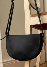 Mustan nahkaisen olkalaukun muoto on puolikuu, sen pinta on sileä ja siinä on vetoketjukiinnitys. Laukussa on ohut ja säädettävä olkaime.