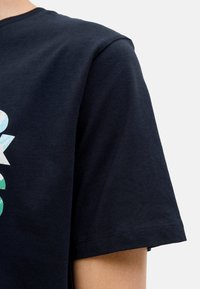 Marineblaue Baumwoll-T-Shirt mit Rundhalsausschnitt, ausgestattet mit einem bunten Grafikdesign auf der Vorderseite. Kurze Ärmel und reguläre Passform.