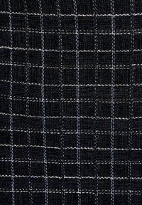 Schwarzer Stoff mit einem Karomuster, das mit weißen Nähten versehen ist. Die Textur wirkt gewebt und verleiht dem Design mit klaren Quadraten Tiefe.