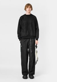 Sudadera negra texturizada con el logo "MWM", combinada con pantalones negros ajustados con bolsillos delanteros y una correa decorativa. Calzado negro.