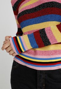 Multicolored sweater featuring horizontal stripes in pink, red, blue, yellow, and black. Textured knit fabric with a fitted design.