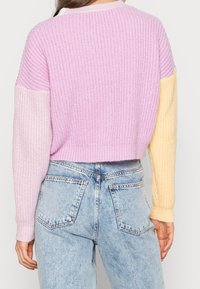 Short-sleeve, cropped sweater with a ribbed texture, featuring light purple, pale pink, and soft yellow colors on the sleeves.